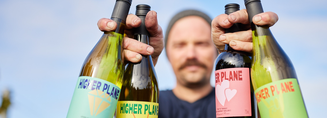 A man holding up Higher Plane wine bottles 